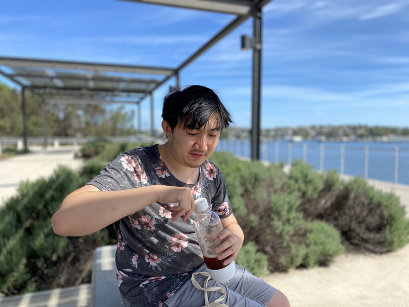 A man, unscrewing a Sodastream bottle with the ocean in the background