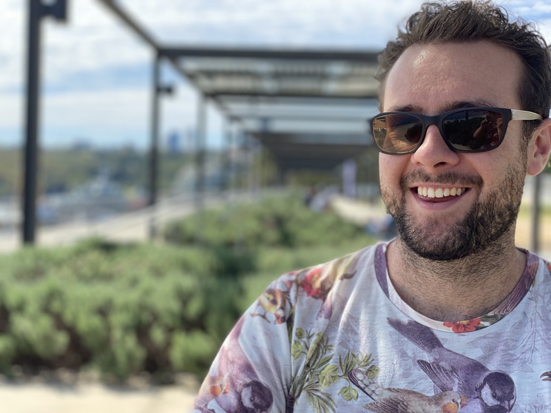 A man, smiling with a garden in the background