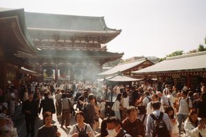 An image of Sensoji temple with many people around it and smoke rising from a small booth in the middle