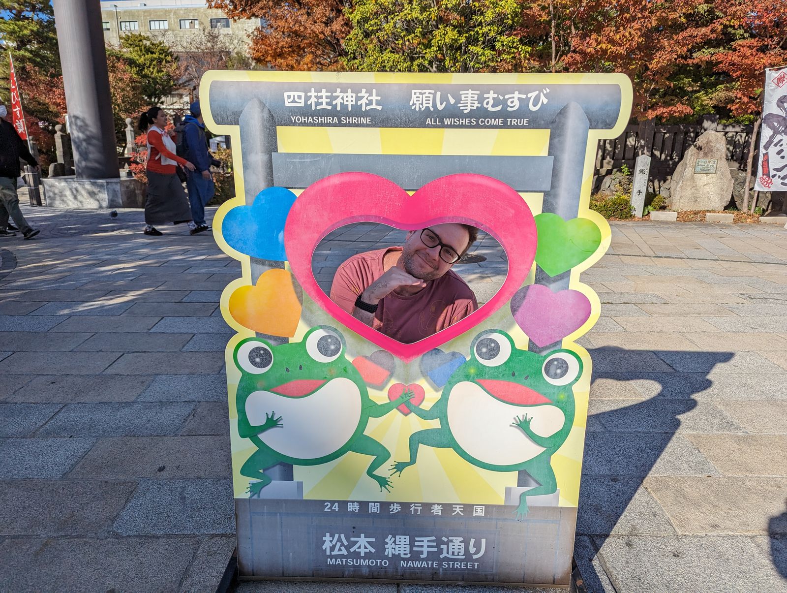 A photo of a person smiling in a cutout with two frogs in the cutout.